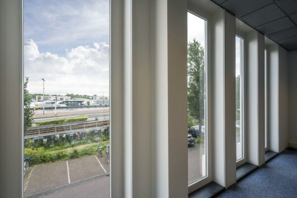 Uitzicht vanuit een kantoorgebouw aan de De Ruijterkade op treinsporen, een perron en een modern stationsgebouw.